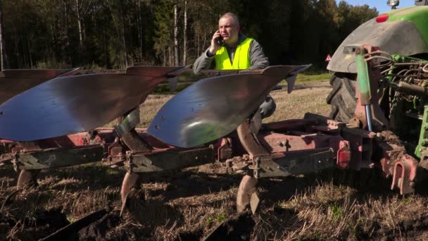 Farmer talking on phone near tractor with plow — Stock Video