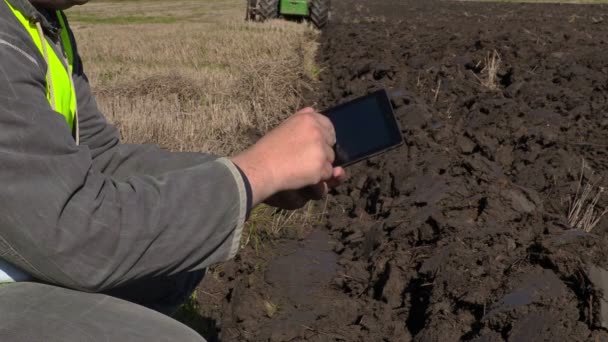 Фермер с планшетным ПК рядом с движущимся трактором на поле — стоковое видео