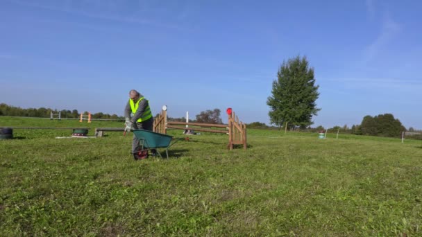 Manipulador de cavalos com carrinho de mão no campo de obstáculos — Vídeo de Stock