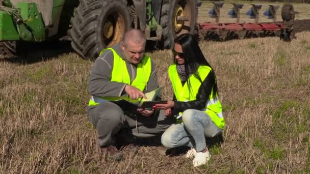 Фермеры говорят и пишут рядом с тракторным пахотным полем — стоковое видео