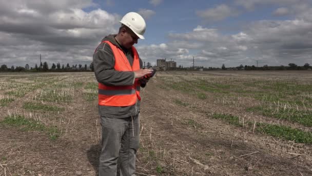 Ingenieur mit Tablet-PC und Fuß auf dem Feld in der Nähe der Fabrik — Stockvideo