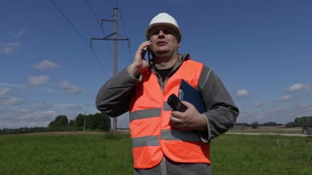 Elingenjör som talar på smartphone under högspänningsledningar — Stockvideo