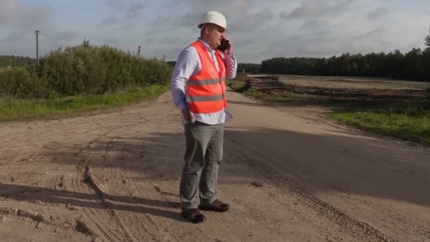 Злой инженер с папкой разговаривает по телефону на сельской дороге — стоковое видео