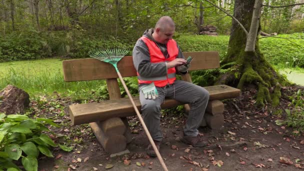 Parkmitarbeiter sitzt auf Bank und bedient Tablet-PC — Stockvideo