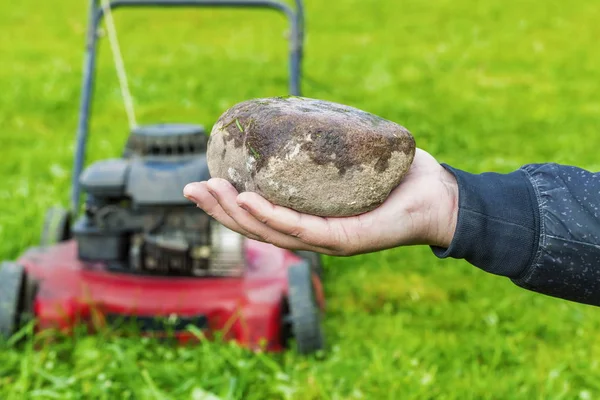 Мужская рука с камнем перед газонокосилкой — стоковое фото