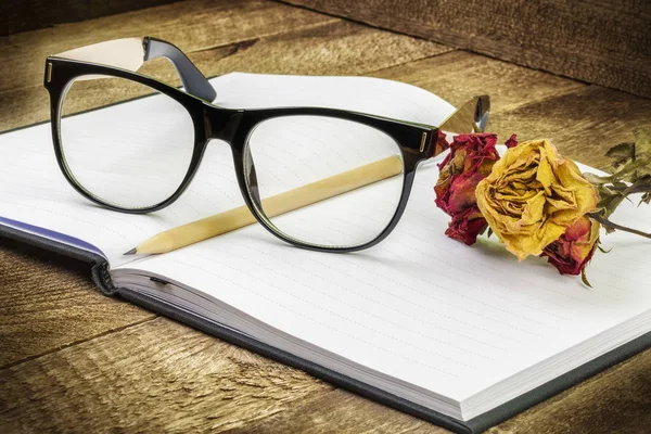 Gafas, cuaderno, bolígrafo y rosas secas — Foto de Stock