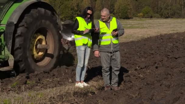 Фермеры говорят и пишут рядом трактор на поле — стоковое видео