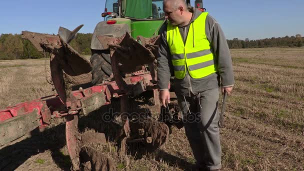 Bauer säubert Pflug neben dem Traktor — Stockvideo