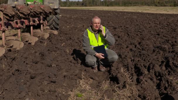 Farmář s dokumentací mluvící smart telefonu poblíž traktor — Stock video