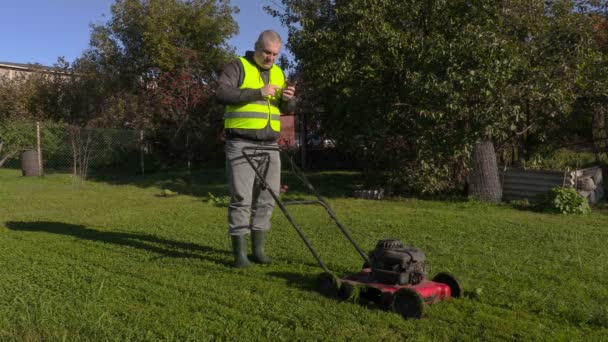 Werknemer praten over telefoon en duwen grasmaaier — Stockvideo