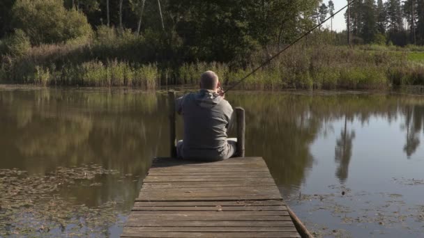 Man sitter på gångbro med fiskespö — Stockvideo