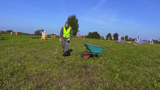 El hombre con escombros de pala recoge residuos en el campo de obstáculos — Vídeo de stock