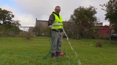 Çim biçme makinesi yakınındaki bahçede sulama adam