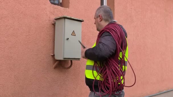 Electricista hablando por teléfono y caja de fusibles abierta cerca de casa — Vídeos de Stock