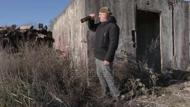 放棄された建物の近くの空のワインの瓶と一緒に酔った男 — ストック動画
