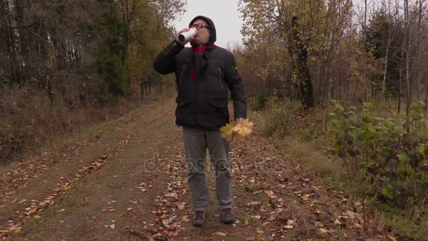 Man with autumn leaves holding cup with drink and walking — Stock Video