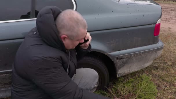 Человек разговаривает по телефону возле застрявшей машины в грязи — стоковое видео