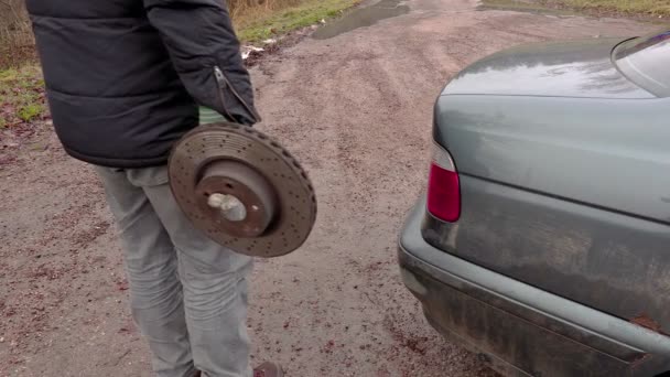 Mann hält alte Bremsscheibe neben Auto — Stockvideo