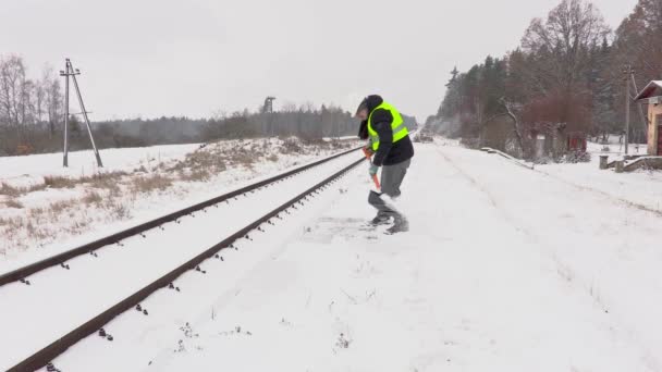 Сотрудник железной дороги чистит снег возле платформы — стоковое видео