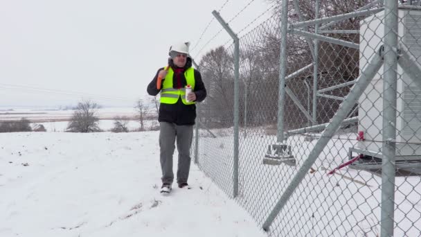 Werknemer met sneeuw shovel wandelen in de buurt van hek en beginnen met drinken thee — Stockvideo