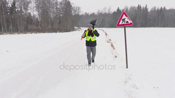 Працівник зі сніжною лопатою в сніжний день біля дорожнього знаку — стокове відео