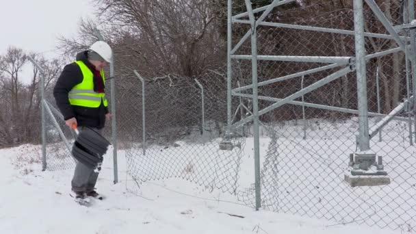 Рабочий с лопатой для снега возле сломанного забора — стоковое видео