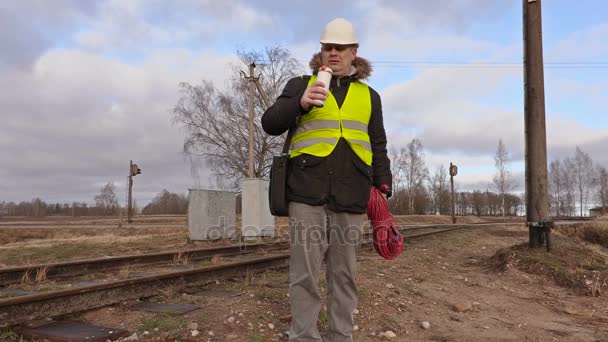Vasúti villanyszerelő kávét iszik közelében railway — Stock videók