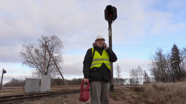 Elettrotecnico ferroviario con cavo che parla al telefono vicino al segnale sulla ferrovia — Video Stock