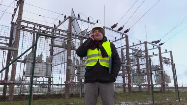 Ingeniero electricista hablando por teléfono inteligente cerca de la subestación en invierno — Vídeos de Stock