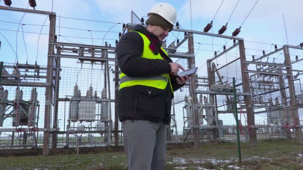 Инженер-электрик фотографирует на планшете возле подстанции зимой — стоковое видео
