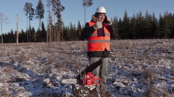 Lumberjack near chainsaw talking on smart phone in forest — Stock Video