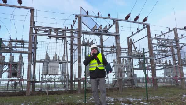 Инженер-электрик ходит и пользуется смартфоном рядом с подстанцией зимой — стоковое видео