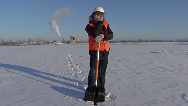 Εργαζόμενος με χιόνι showel στο χιόνι που καλύπτει πεδίο κοντά στο εργοστάσιο — Αρχείο Βίντεο