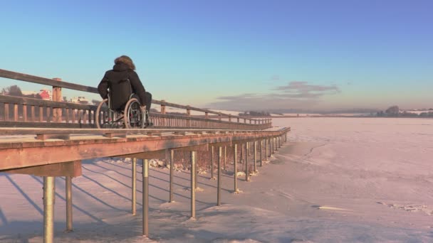 Postižený člověk na vozíku na pěší most u jezera — Stock video