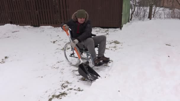 Bărbat cu handicap în scaun cu rotile care lucrează cu lopată de zăpadă — Videoclip de stoc