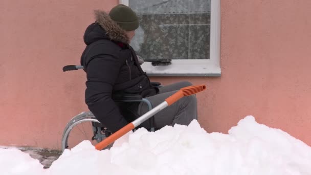 Disabled man on wheelchair cleaning window from the snow — Stock Video