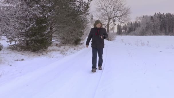 Man met professionele fotocamera op sneeuw bedekte weg in de winter — Stockvideo