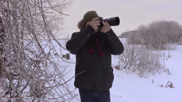 Мужчина фотографирует на профессиональную фотокамеру зимой — стоковое видео