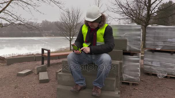 Trabalhador sentado em tijolos de pavimentação e usando tablet — Vídeo de Stock