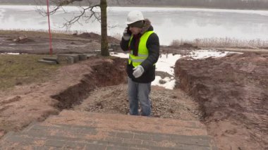 Bitmemiş kaldırım yakınındaki akıllı telefonda konuşurken inşaat mühendisi