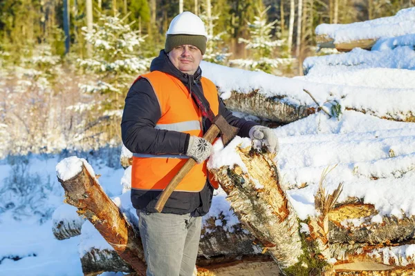 Lumberjack with ax near pile of logs in winter — Stock Photo, Image