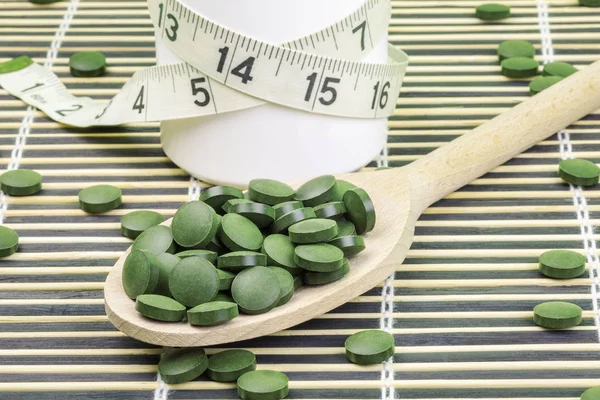 Spirulina, chlorela pílulas na colher de madeira e fita métrica — Fotografia de Stock