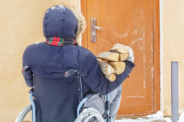 Behinderter im Rollstuhl vor Tür mit Brennholzstämmen — Stockfoto