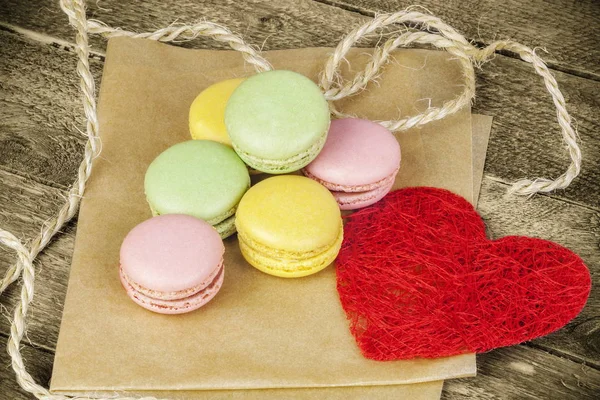 Macarons в різних кольорів на папері, поблизу червоного паперу серця — стокове фото