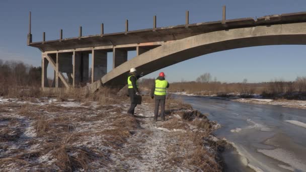 Инженеры разговаривают и идут рядом с мостом — стоковое видео