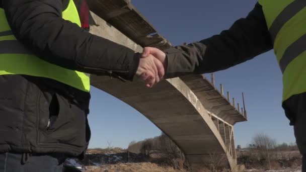 Ingenieros estrechando manos cerca del puente inacabado — Vídeos de Stock
