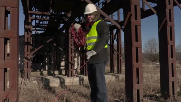 Рабочие собирают шнур питания возле металлических резервуаров — стоковое видео