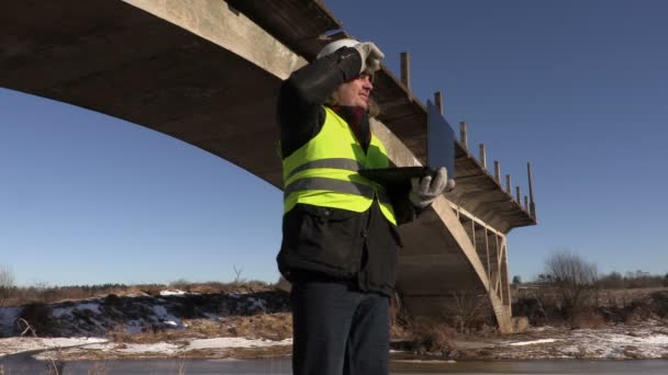 Ingenieur im Winter mit Laptop in der Nähe der Brücke — Stockvideo