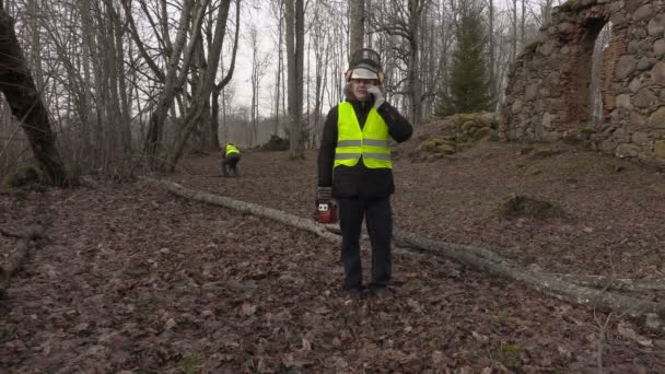 Arbetare med motorsåg och telefonen nära fallna träd — Stockvideo