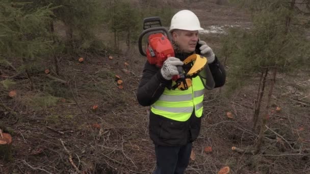 Worker with chainsaw on shoulder talking on phone on  steep forest slope — Stock Video